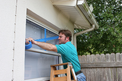 man on ladder taping a window with blue tape for a storm